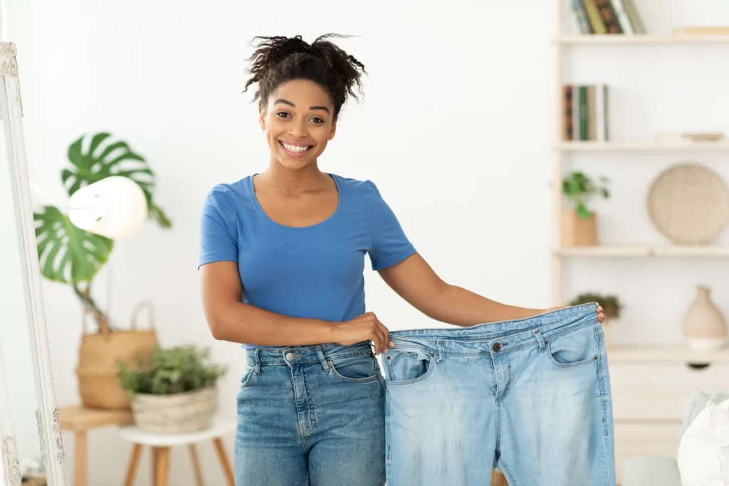 happy woman holding oversized jeans in bright home utc ()